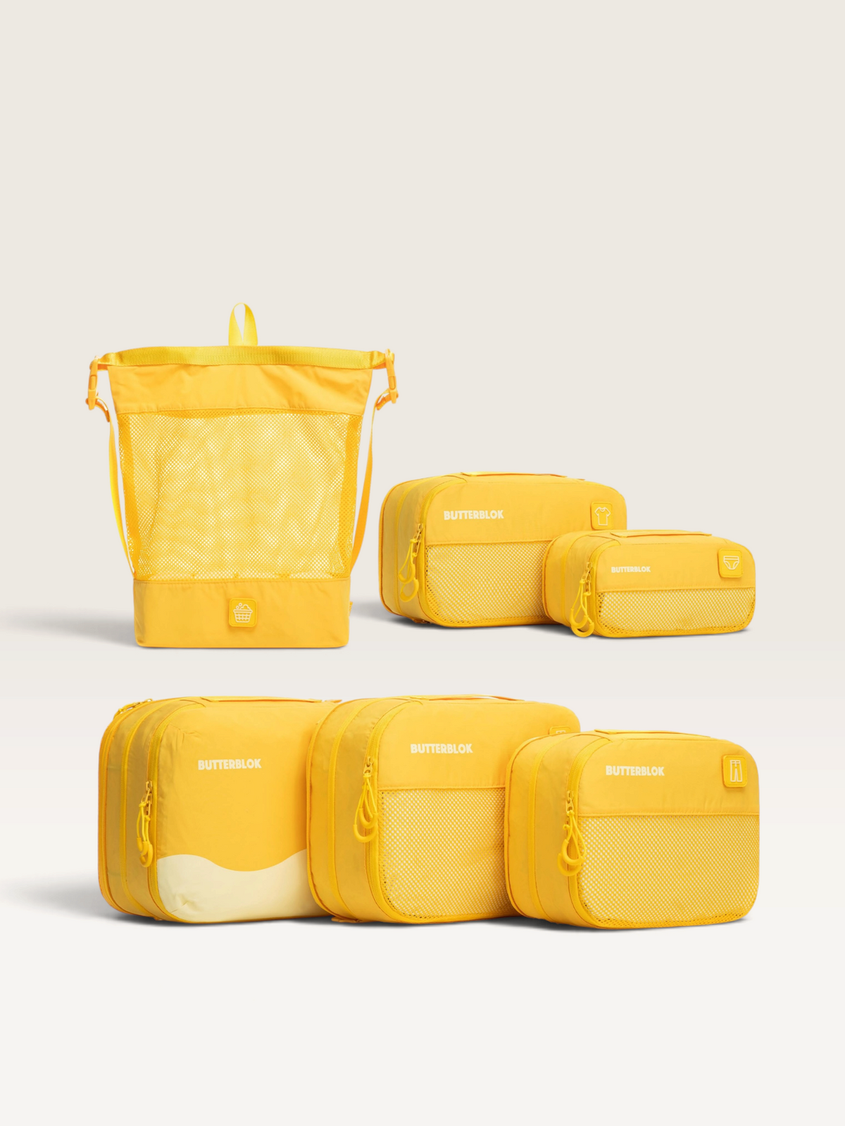 A set of yellow packing cubes and a mesh laundry bag from the brand Butterbloss, arranged on a clean off-white background.