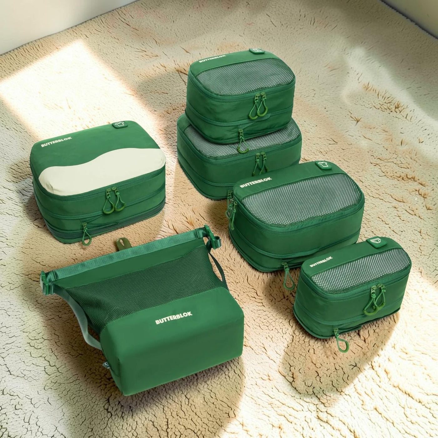 Green Butterblok packing cubes laid out on warm sand