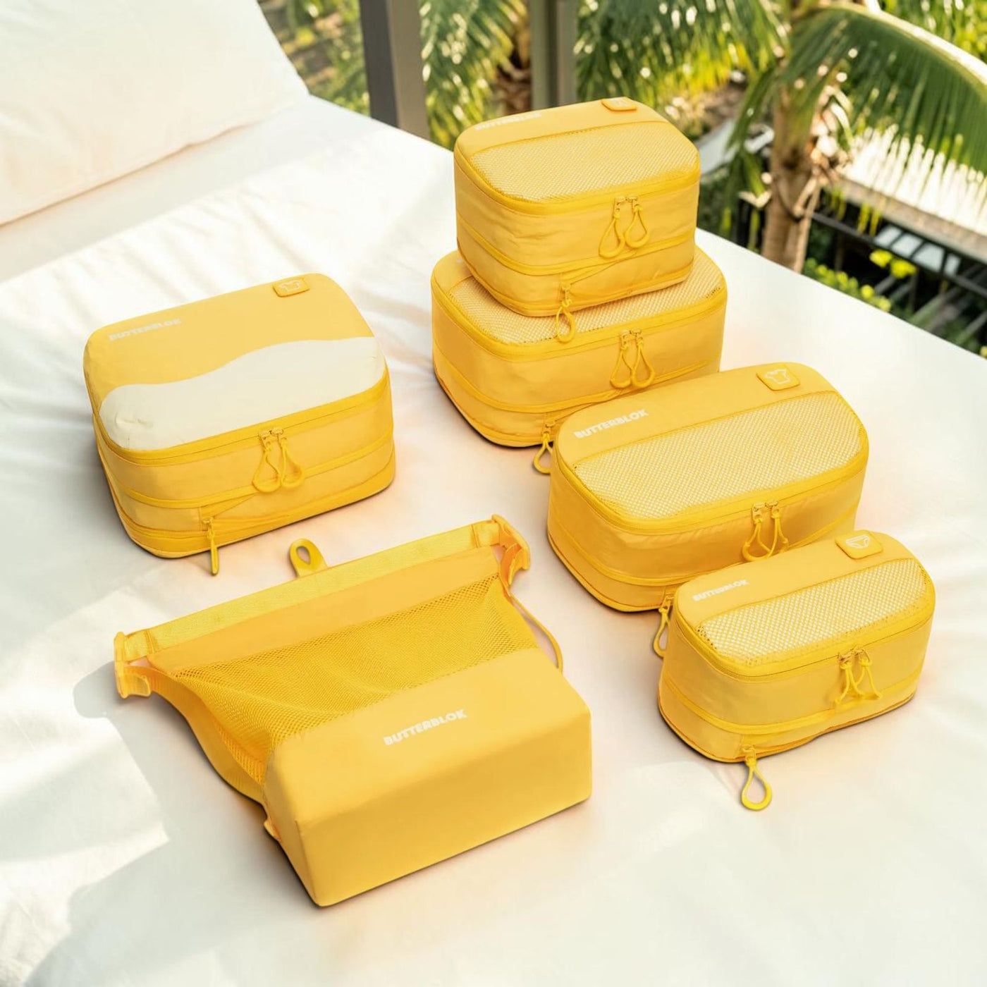 Six yellow Butterblok packing cubes on a daybed beside a pool