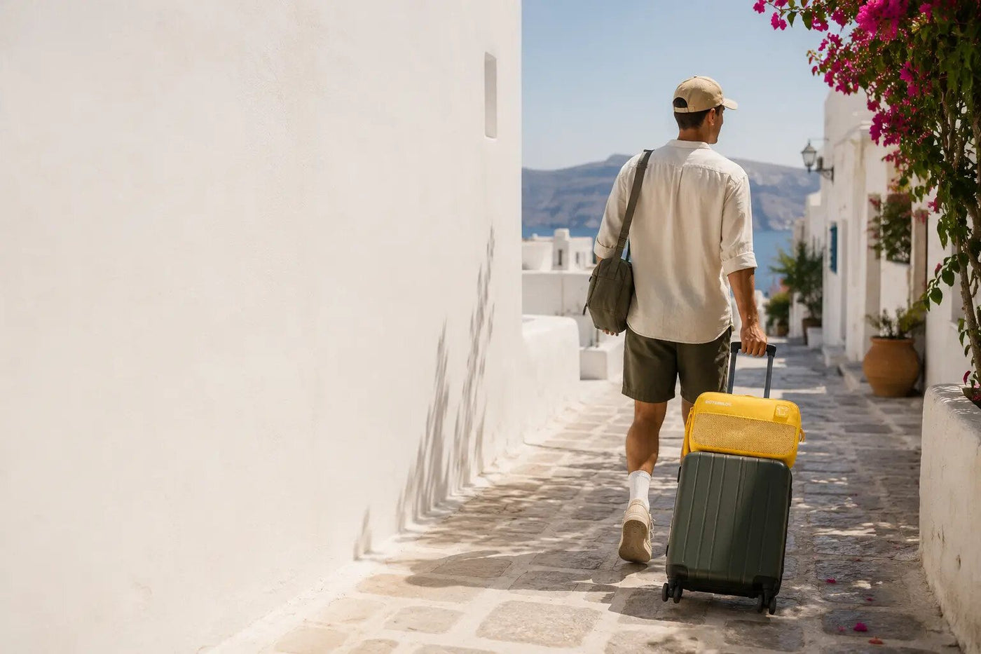 A traveller walking a suitcase through a sunlit street